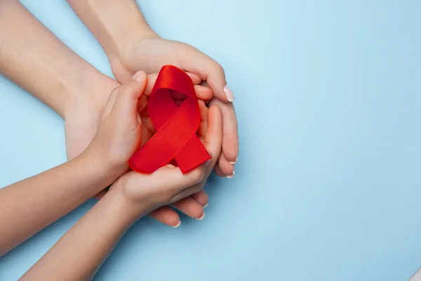 Женские и мужские руки с красной лентой информирования о ВИЧ и СПИДе изолированы на синем фоне — стоковое фото