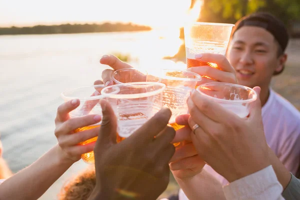 Groupe d'amis cliquetis de verres à bière pendant le pique-nique à la plage. Style de vie, amitié, plaisir, week-end et concept de repos. — Photo