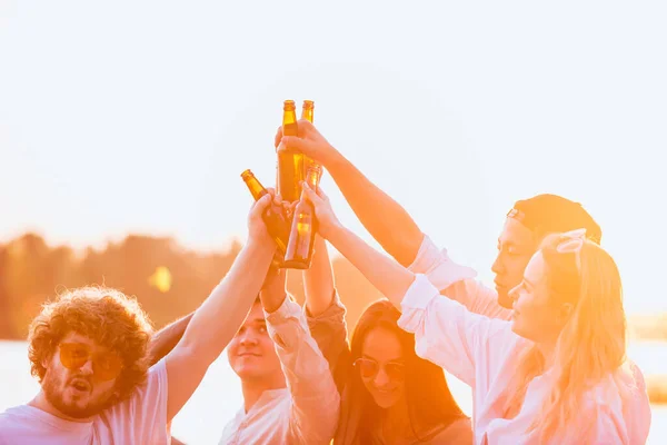 Grupo de amigos batendo copos de cerveja durante piquenique na praia. Estilo de vida, amizade, diversão, fim de semana e conceito de descanso . — Fotografia de Stock