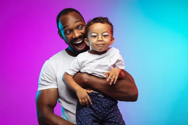 African-american father and son portrait on gradient studio background in neon