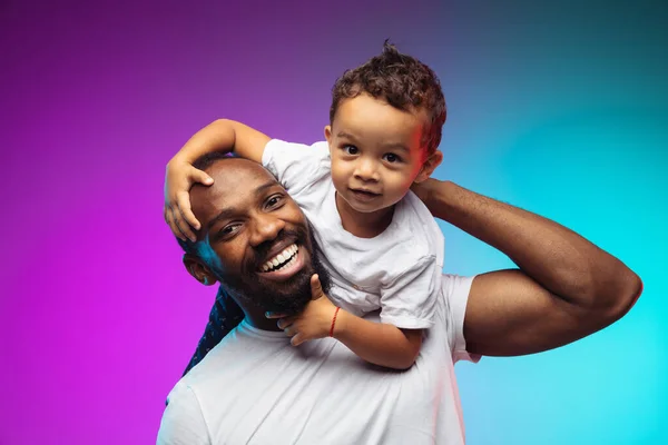Афро-американский портрет отца и сына на градиентном фоне студии в неоновом — стоковое фото