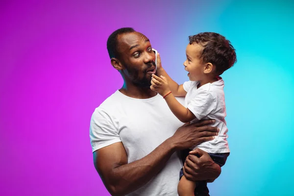 Afro-Amerikaanse vader en zoon portret op gradiënt studio achtergrond in neon — Stockfoto