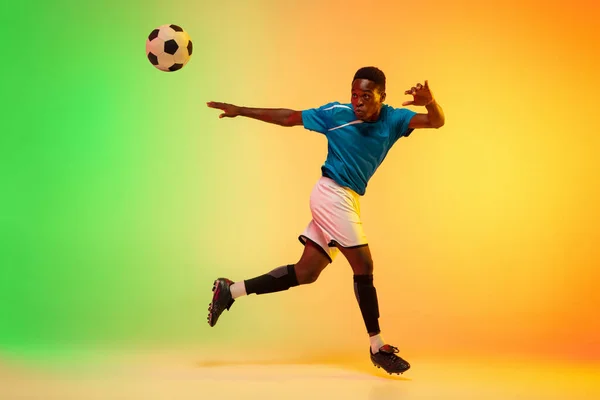 Futebol masculino, jogador de futebol treinando em ação isolado no fundo do estúdio gradiente em luz de néon — Fotografia de Stock