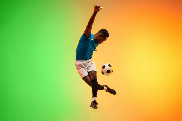 Mężczyzna piłka nożna, piłkarz trening w akcji odizolowany na gradientowym tle studio w świetle neonu — Zdjęcie stockowe