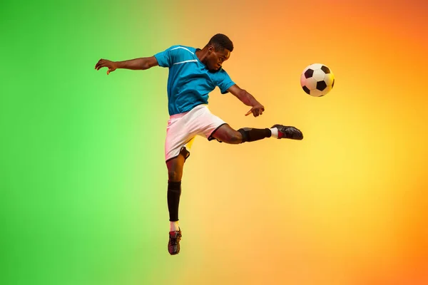 Futebol masculino, jogador de futebol treinando em ação isolado no fundo do estúdio gradiente em luz de néon — Fotografia de Stock