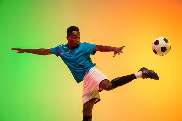 Mężczyzna piłka nożna, piłkarz trening w akcji odizolowany na gradientowym tle studio w świetle neonu — Zdjęcie stockowe