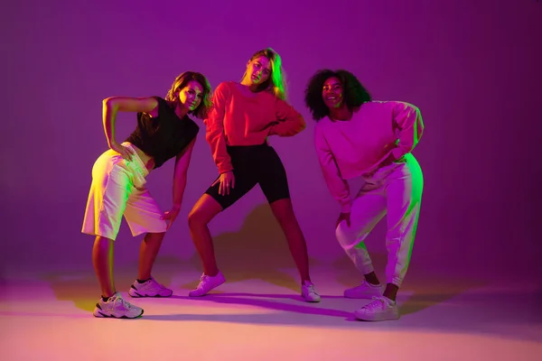 Chicas deportivas bailando hip-hop con ropa elegante sobre fondo degradado en la sala de baile en luz de neón — Foto de Stock