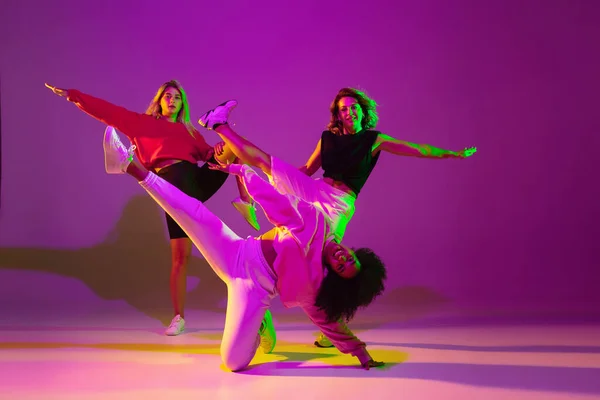 Sportive girls dancing hip-hop in stylish clothes on gradient background at dance hall in neon light — Stock Photo, Image