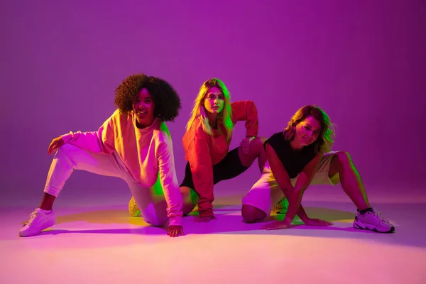 Meninas esportivas dançando hip-hop em roupas elegantes no fundo gradiente no salão de dança em luz de néon — Fotografia de Stock