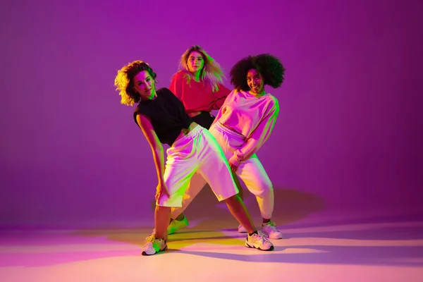 Meninas esportivas dançando hip-hop em roupas elegantes no fundo gradiente no salão de dança em luz de néon — Fotografia de Stock