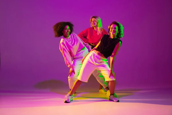 Sportive girls dancing hip-hop in stylish clothes on gradient background at dance hall in neon light — Stock Photo, Image