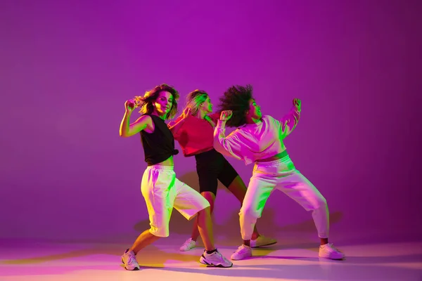 霓虹灯下的舞厅里，穿着时髦衣服、穿着渐变背景的活泼姑娘们正在跳嘻哈舞 — 图库照片