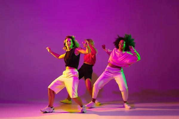 Meninas esportivas dançando hip-hop em roupas elegantes no fundo gradiente no salão de dança em luz de néon — Fotografia de Stock