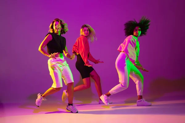 Meninas esportivas dançando hip-hop em roupas elegantes no fundo gradiente no salão de dança em luz de néon — Fotografia de Stock