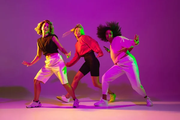 Meninas esportivas dançando hip-hop em roupas elegantes no fundo gradiente no salão de dança em luz de néon — Fotografia de Stock