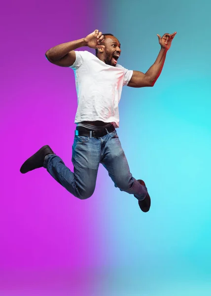 African-american young mans portrait on gradient studio background in neon, jumping high