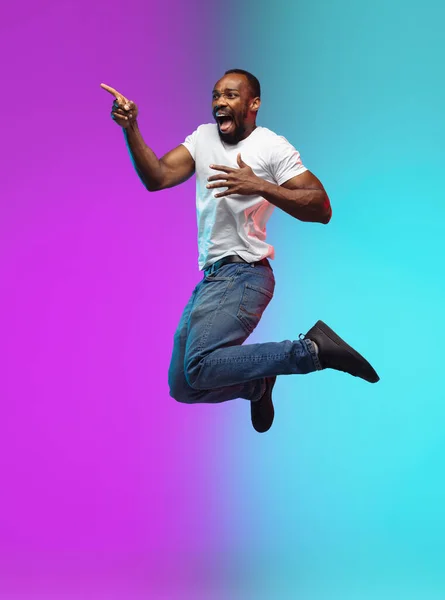 African-american young mans portrait on gradient studio background in neon, jumping high — Stock Photo, Image