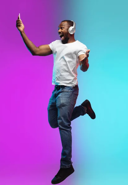 Afro-americano joven mans retrato en gradiente estudio fondo en neón, saltar alto — Foto de Stock