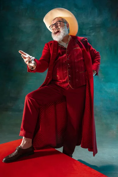 Современный стильный Санта-Клаус в красном модном костюме и ковбойской шляпе на тёмном фоне — стоковое фото
