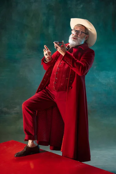 Modern stylish Santa Claus in red fashionable suit and cowboys hat on dark background — Stock Photo, Image