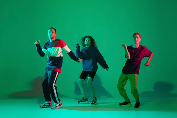 Stijlvolle mannen en vrouwen dansen hip-hop in heldere kleren op gradiënt achtergrond in danszaal in neon licht — Stockfoto