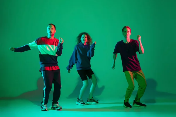 Stylish men and woman dancing hip-hop in bright clothes on gradient background at dance hall in neon light
