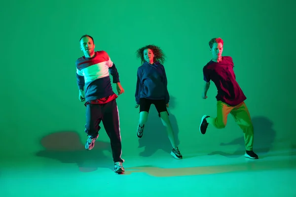 Stijlvolle mannen en vrouwen dansen hip-hop in heldere kleren op gradiënt achtergrond in danszaal in neon licht — Stockfoto