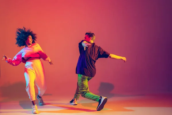 Stylish man and woman dancing hip-hop in bright clothes on gradient background at dance hall in neon light — Stock Photo, Image