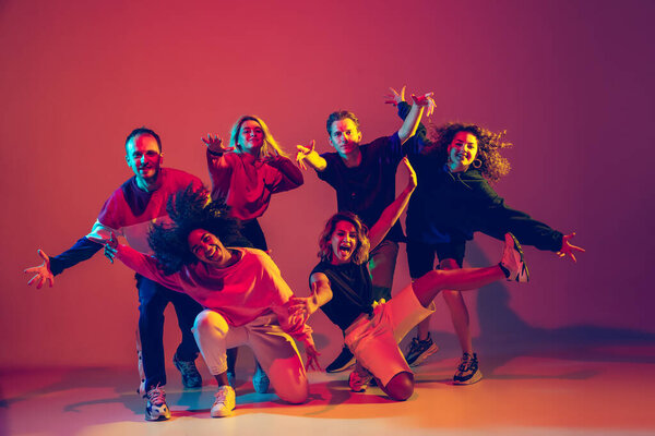 Стильные мужчины и женщины танцуют хип-хоп в яркой одежде на градиентном фоне в танцевальном зале в неоновом свете