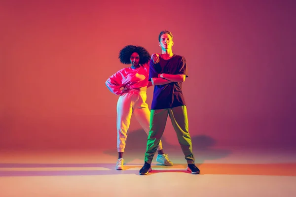Stílusos férfi és nő táncol hip-hop fényes ruhákban gradiens háttér táncterem neon fény — Stock Fotó