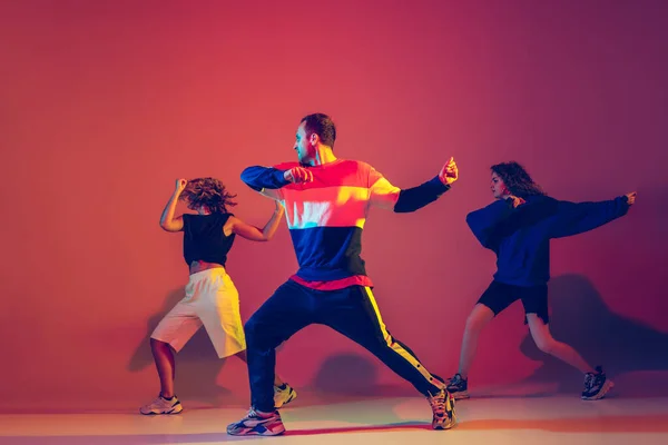Stijlvolle man en vrouw dansen hip-hop in heldere kleren op gradiënt achtergrond in danszaal in neon licht — Stockfoto