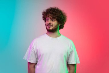 Beyaz tenli genç adam, neon renkli gradyan stüdyo arka planında portre çiziyor.