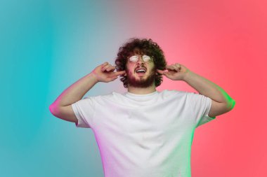 Beyaz tenli genç adam, neon renkli gradyan stüdyo arka planında portre çiziyor.