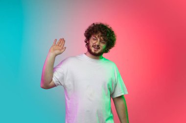 Beyaz tenli genç adam, neon renkli gradyan stüdyo arka planında portre çiziyor.