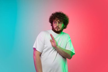 Beyaz tenli genç adam, neon renkli gradyan stüdyo arka planında portre çiziyor.