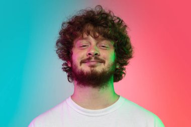 Beyaz tenli genç adam, neon renkli gradyan stüdyo arka planında portre çiziyor.