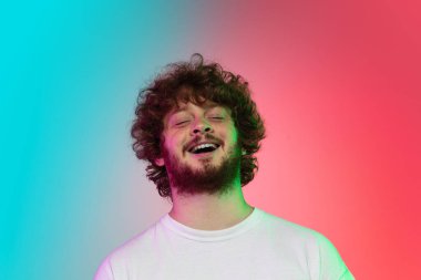 Beyaz tenli genç adam, neon renkli gradyan stüdyo arka planında portre çiziyor.