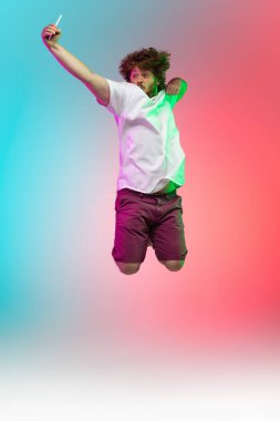 Beyaz tenli genç adam, neon renkli gradyan stüdyo arka planında portre çiziyor.