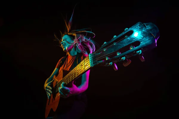 Playing guitar. Young woman with smoke and neon light on black background. Highly tensioned, wide angle, fish eye view