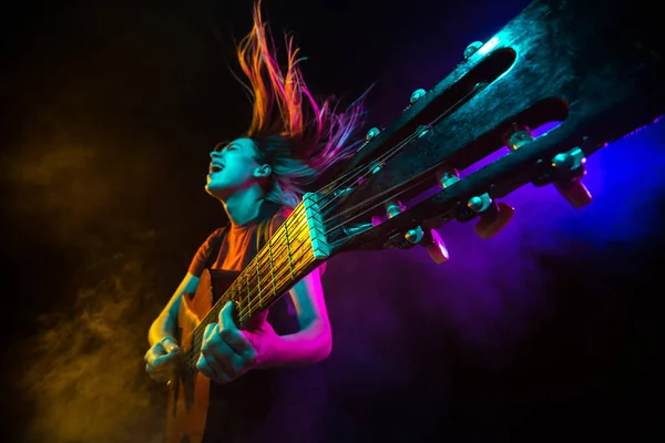 Gitarre spielen. Junge Frau mit Rauch und Neonlicht auf schwarzem Hintergrund. Hochgespannt, Weitwinkel, Fischaugenblick — Stockfoto