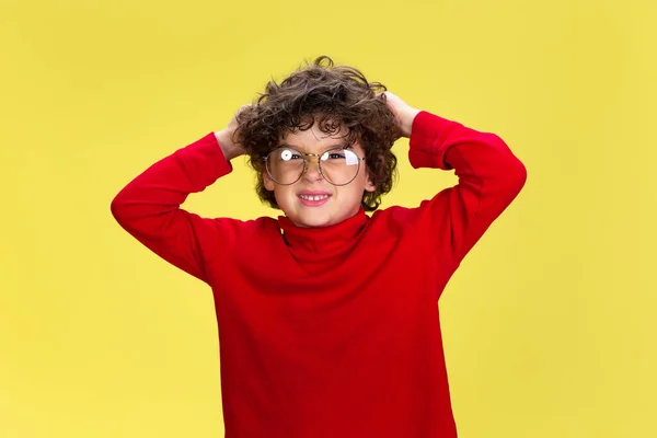 Muito jovem menino encaracolado em vermelho desgaste no fundo do estúdio amarelo. Infância, expressão, diversão. — Fotografia de Stock