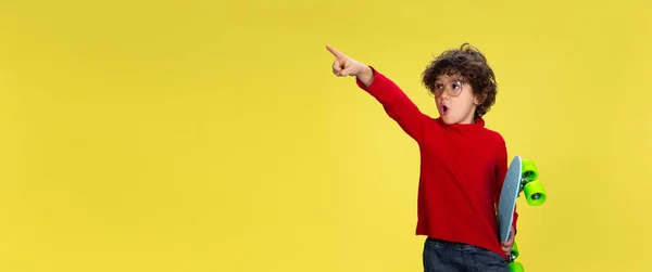 Ładny młody kręcony chłopiec w czerwonym stroju na żółtym tle studio. Dzieciństwo, ekspresja, zabawa. — Zdjęcie stockowe