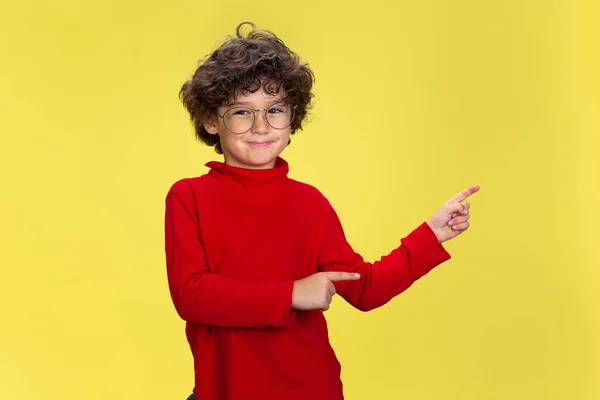 Ganska ung lockig pojke i rött slitage på gul studio bakgrund. Barndom, uttryck, kul. — Stockfoto
