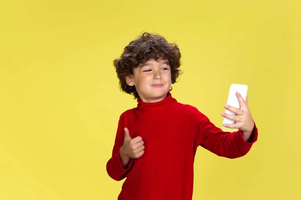 Joli jeune garçon bouclé en tenue rouge sur fond de studio jaune. Enfance, expression, plaisir. — Photo