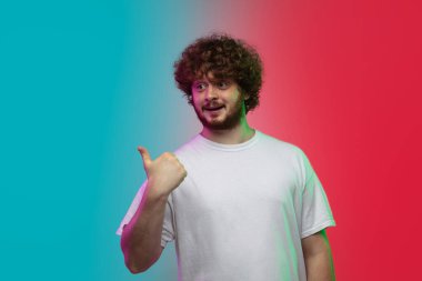 Beyaz tenli genç adam, neon renkli gradyan stüdyo arka planında portre çiziyor.