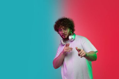 Beyaz tenli genç adam, neon renkli gradyan stüdyo arka planında portre çiziyor.