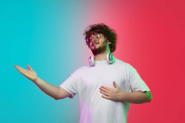 Beyaz tenli genç adam, neon renkli gradyan stüdyo arka planında portre çiziyor.