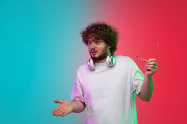 Beyaz tenli genç adam, neon renkli gradyan stüdyo arka planında portre çiziyor.