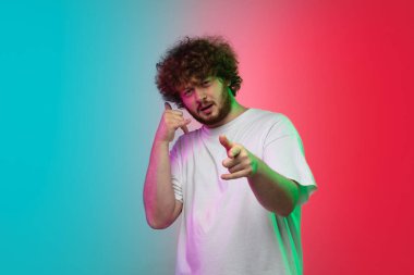 Beyaz tenli genç adam, neon renkli gradyan stüdyo arka planında portre çiziyor.