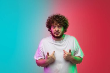 Beyaz tenli genç adam, neon renkli gradyan stüdyo arka planında portre çiziyor.